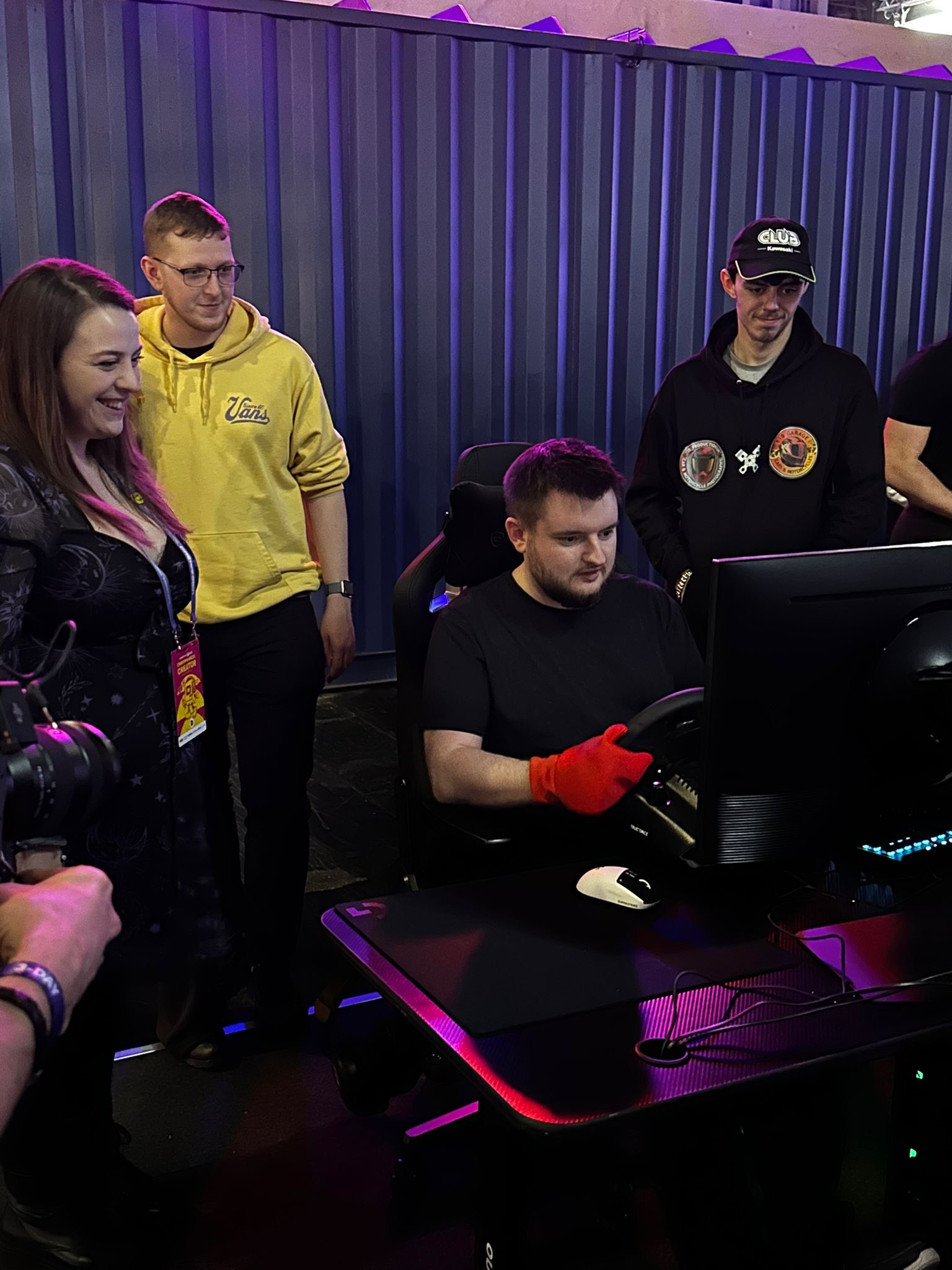 Smilar at the wheel of a racing simulator, with other attendees watching